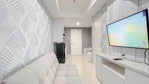 Una sala de estar moderna con un sofá, un televisor de pantalla plana montado en la pared y una cocina al fondo.
