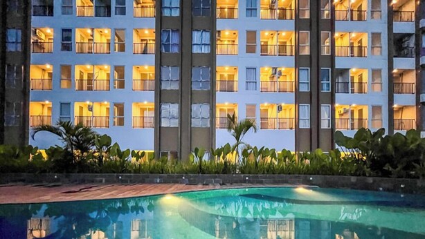 Un hotel de varios pisos con balcones, piscina y zonas verdes al frente.