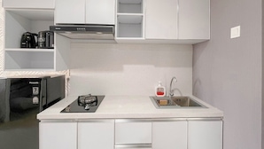 Una cocina compacta con armarios blancos, estufa integrada, lavabo y cafetera.