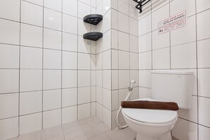 Un bagno con pareti piastrellate in bianco, un WC bianco e una zona doccia con accessori neri.