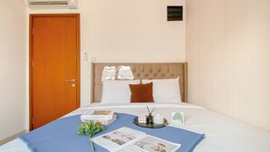 A hotel room with a bed, a wooden door, an air conditioning unit, and a small window. - Soft Urban Living 2Br At Signature Park Grande Apartment (Jakarta)
