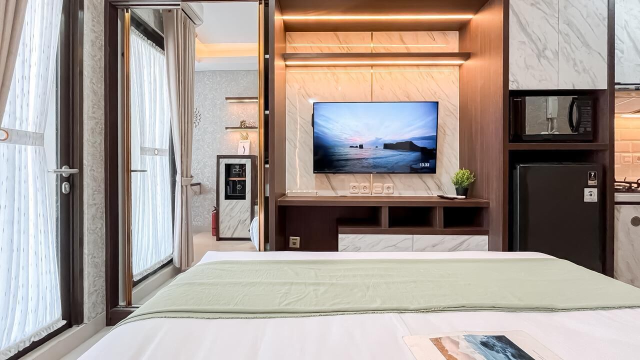 A hotel room with a large bed, a TV mounted on the wall, a small kitchen area, and a bathroom visible through an open door.