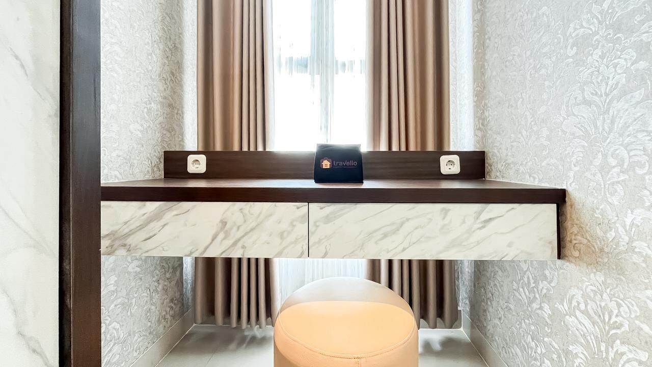 Une chambre d’hôtel avec un meuble-lavabo en marbre, une petite table sur laquelle se trouve un porte-documents de voyage, et une fenêtre avec des rideaux.