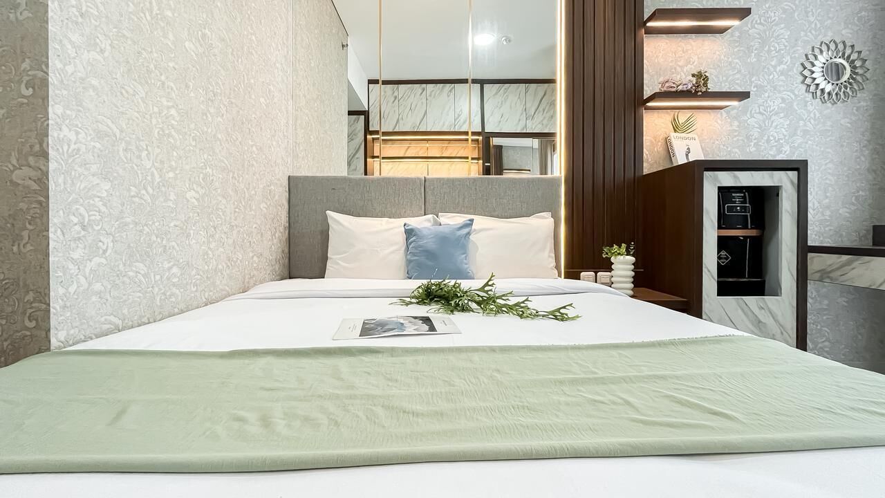 A neatly made bed with a green throw, a headboard, and a bedside table with a plant.