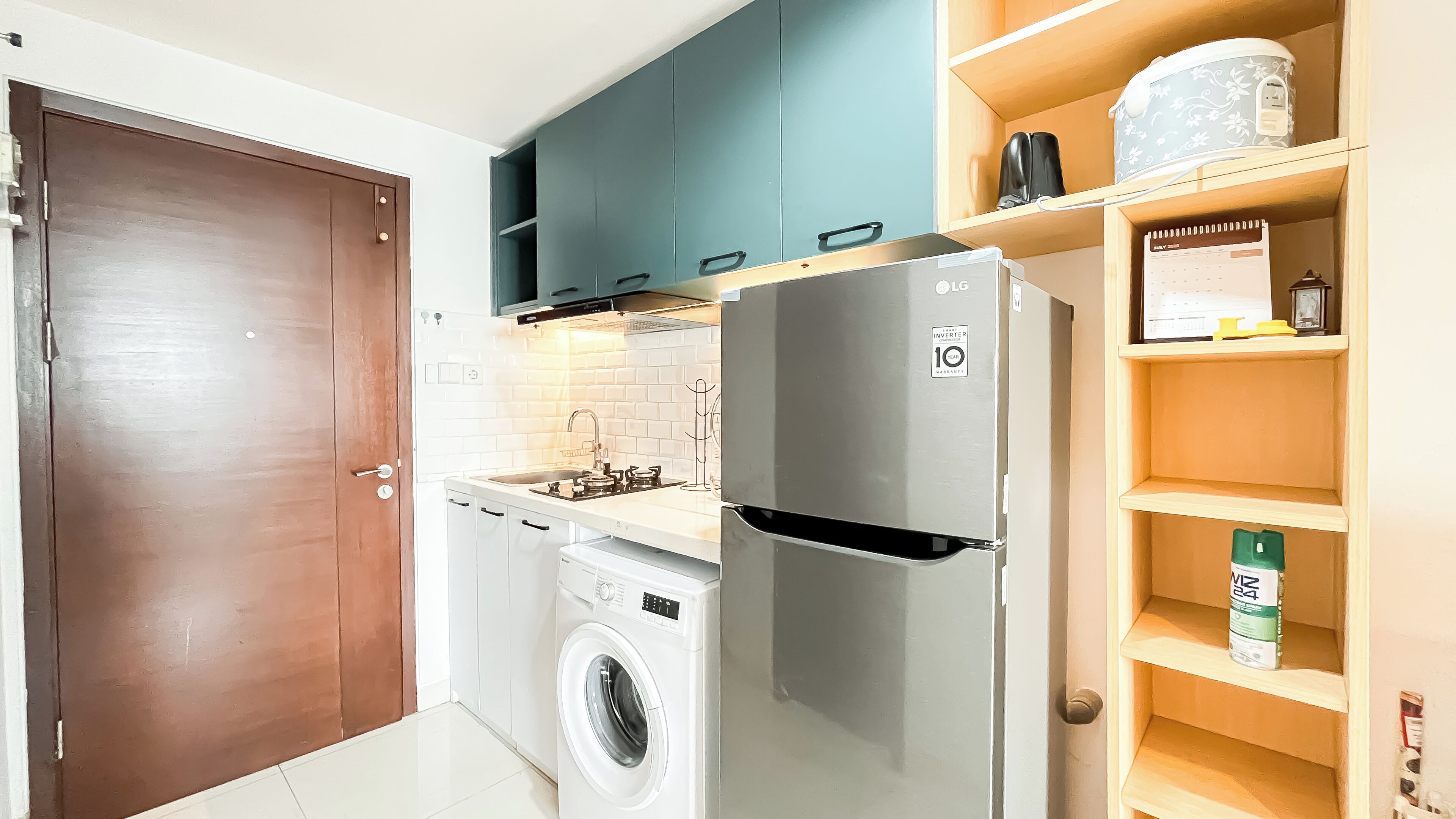 A compact kitchen with a washing machine, a refrigerator, and a wooden shelf with a calendar.