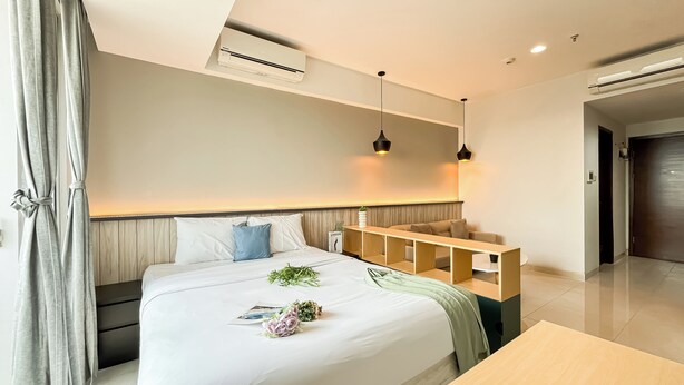 A modern hotel room with a bed, bedside tables, a small seating area, and an air conditioning unit. - Spacious Studio Apartment West Vista Near Rawa Buaya Station (Jakarta)