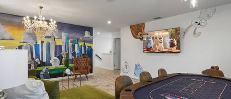 Una habitación con mesa de billar, sofás verdes, una lámpara de araña y un mural de paisaje urbano.