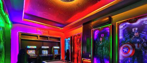 A pool table in a room with colorful lighting and posters of Marvel characters.