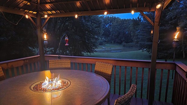 Eine überdachte Terrasse im Freien mit einem runden Tisch, Stühlen, einer Feuerstelle und Lichterketten.
