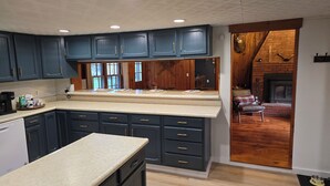 A kitchen with dark blue cabinets, a large island, and a view into a living area with a fireplace.