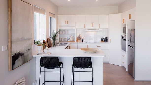 A modern kitchen with white cabinets, a central island with two black chairs, and a large painting on the wall. - Luxe Retreat in Battery Point (Battery Point)