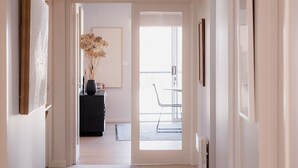 A hallway with a carpeted floor, white walls, and a ceiling light. There is a door at the end leading to a balcony with a chair and a table. - Luxe Retreat in Battery Point (Battery Point)