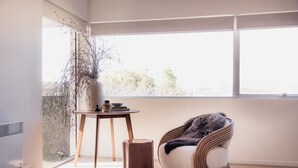 A modern room with a large window, a wicker chair, a small wooden table, and a potted plant. - Luxe Retreat in Battery Point (Battery Point)