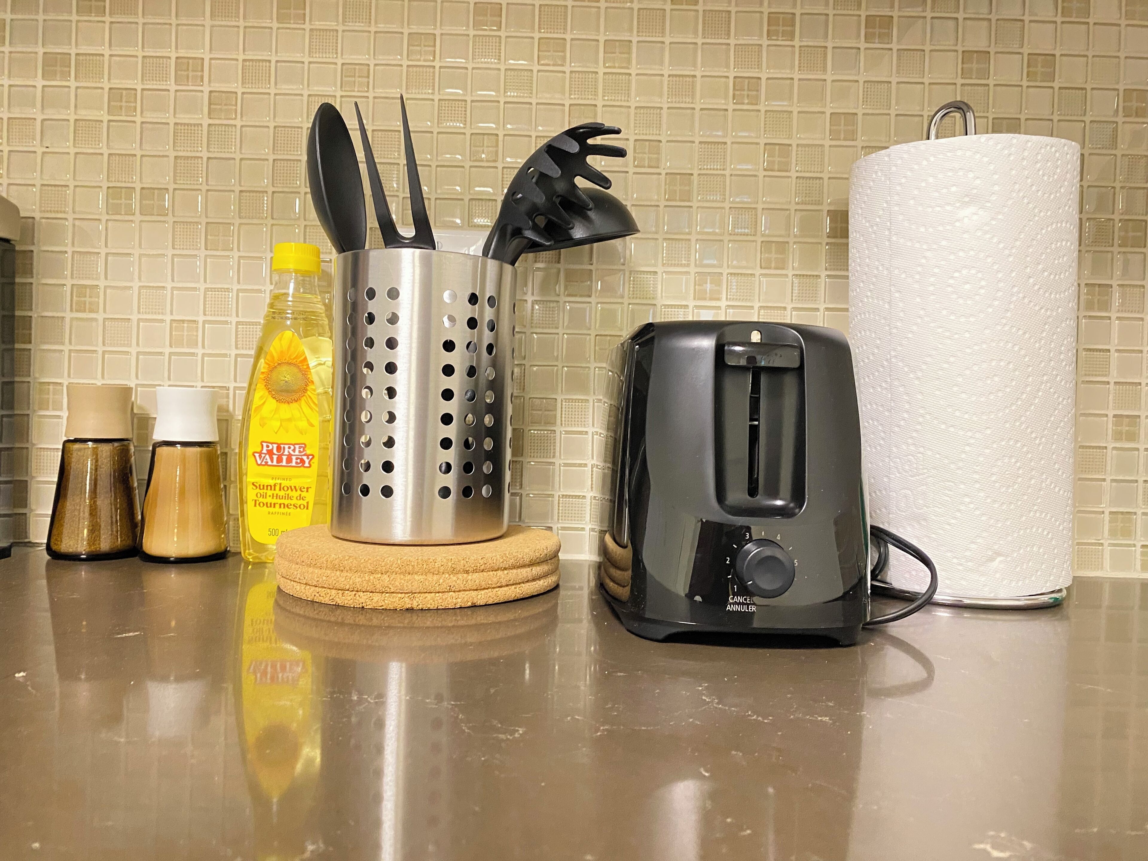 A kitchen counter with a toaster, a paper towel holder, a grater, and two spice bottles.