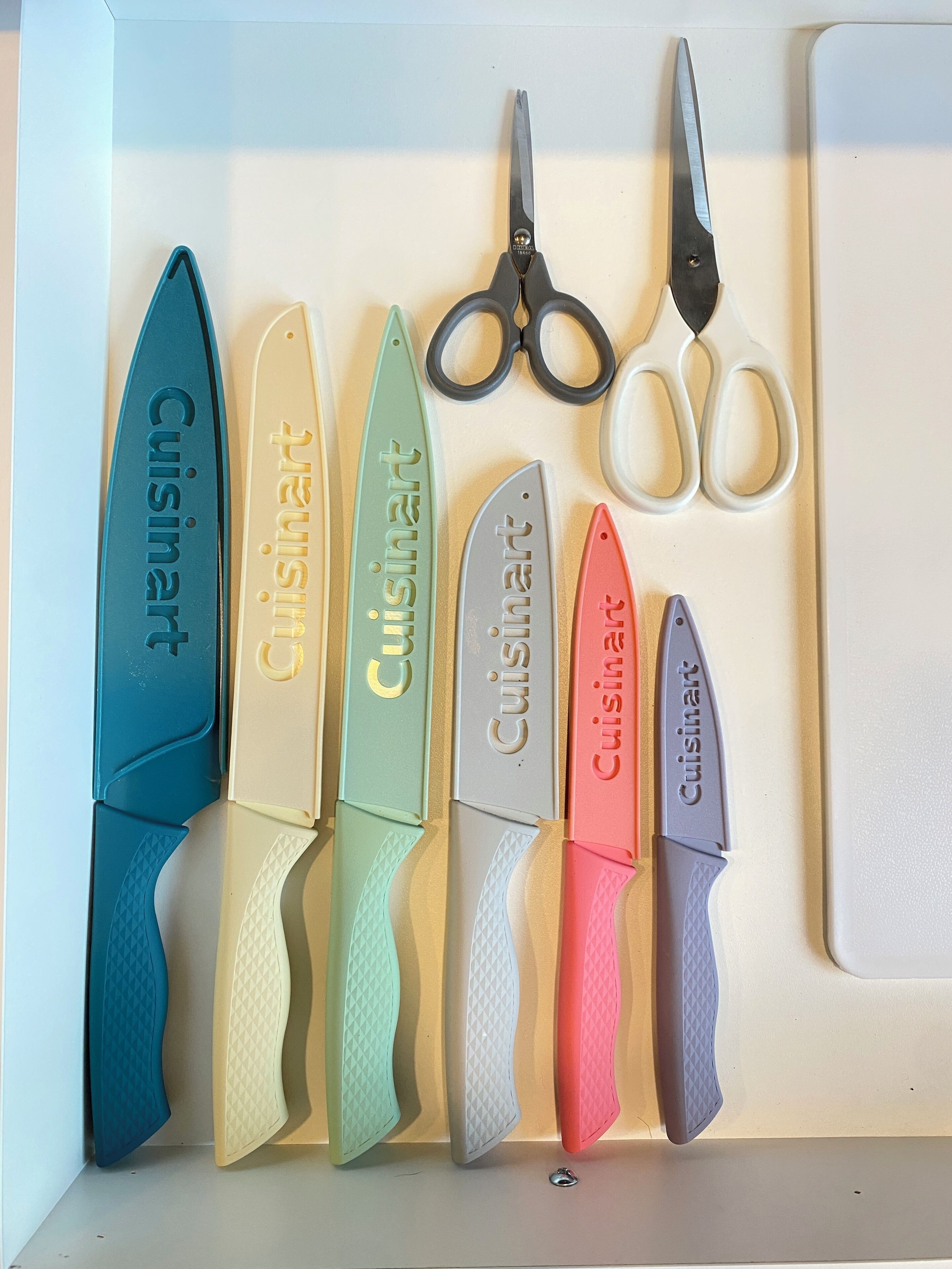 A set of knives and scissors with the brand 'Cuisinart' engraved on them, arranged on a white surface.