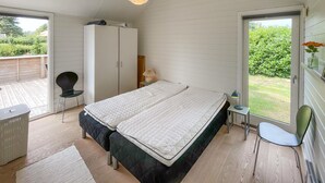 Quarto com cama grande, guarda-roupa, escrivaninha com candeeiro e vista para um jardim através de uma porta deslizante.