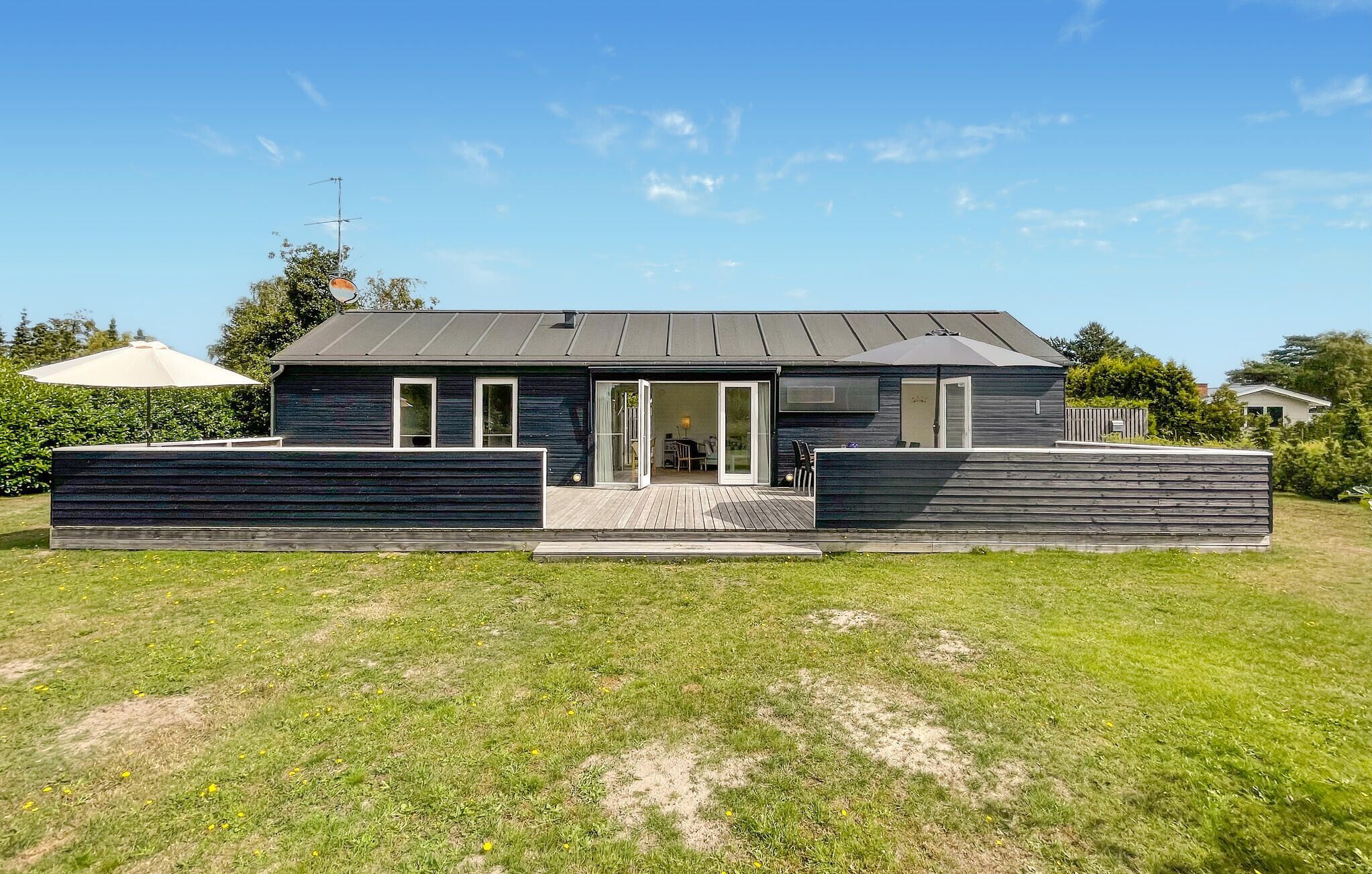 A modern house with a flat roof, large sliding glass doors, and a deck area.
