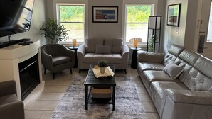 A living room with a fireplace, two sofas, a coffee table, and a TV. - Golf, Beach & Great Local Eats! This condo unit is minutes is away from it all. (Breadalbane)