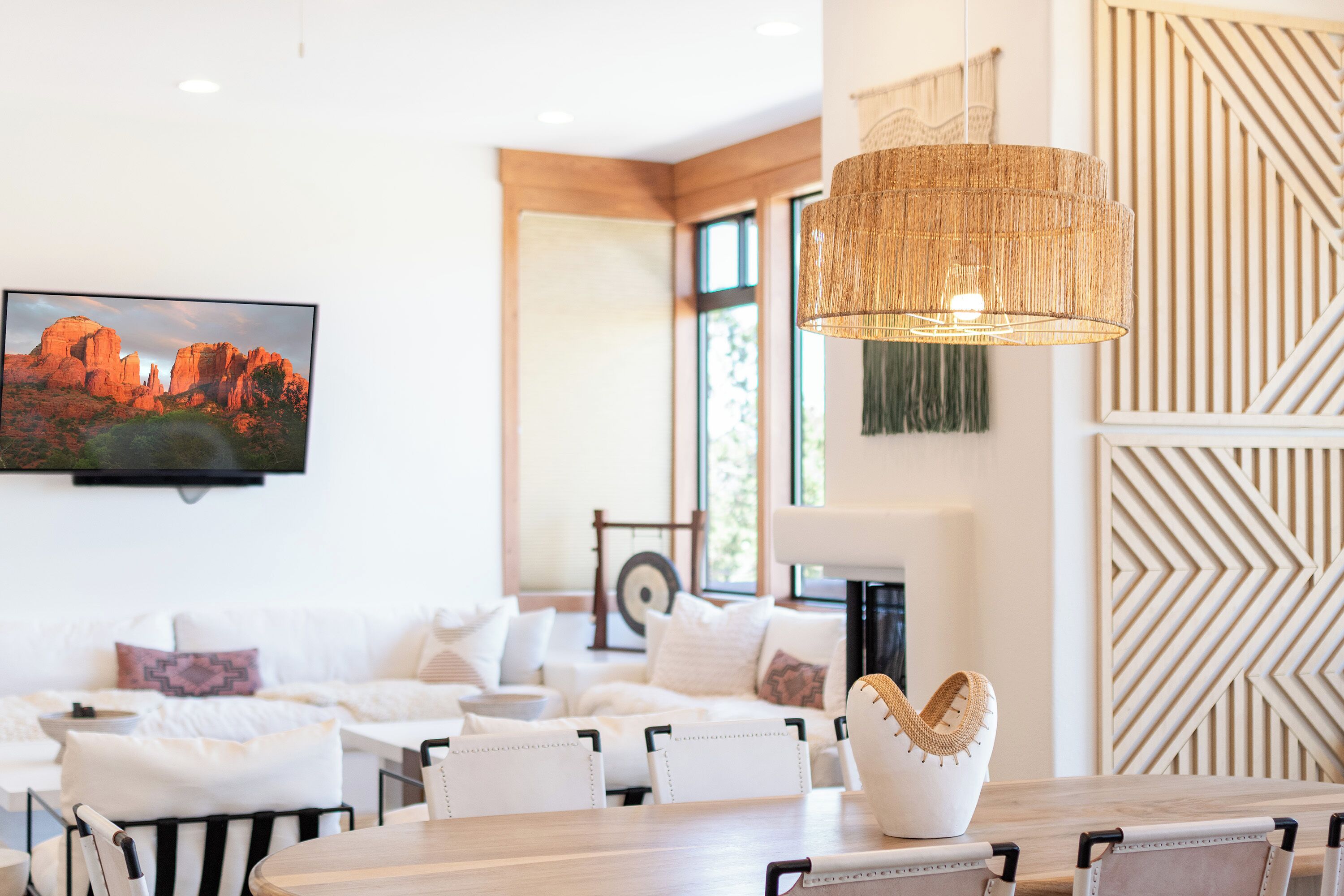 A modern living room with a wooden dining table, white sofas, and a large woven light fixture.