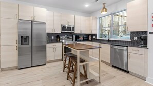 A modern kitchen with stainless steel appliances, a wooden table, and a window with blinds. - 3/3 sauna, arcade, play couch, 70" TV, fire pit, balconies, 6 min from downtown (Chattanooga)