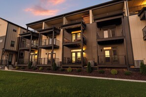 A multi-story residential building with balconies, a covered front porch, and a landscaped front yard.