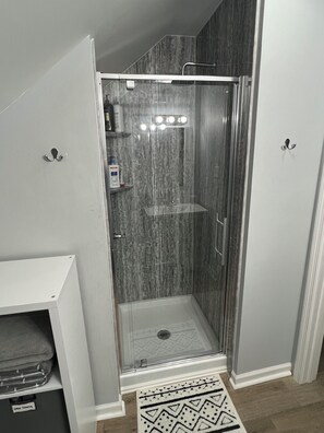 A walk-in shower with a glass door, a showerhead, and a light fixture. - Cozy, pet-friendly, 1-bedroom apartment in Oak Ridge with AC (Oak Ridge)