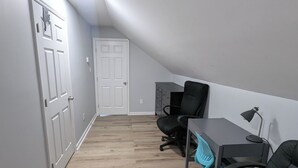 Un couloir étroit avec un plafond en pente, un plancher en bois et une porte blanche au fond.