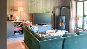 A cozy living room with a sofa, a flat-screen TV, a wooden wall, a fireplace, and a window with curtains. - 3 bedroom awesome apartment in Hemsedal (Hemsedal)
