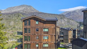 A multi-story wooden building with large windows, set against a mountainous backdrop. - 3 bedroom awesome apartment in Hemsedal (Hemsedal)