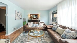 A living room with two brown leather sofas, a glass coffee table, and a floral painting on the wall.