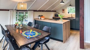 Un coin repas avec une table en bois, des chaises et un jeu de société. Il y a également un coin cuisine équipé d’un four à micro-ondes et d’un évier.