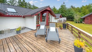 Une terrasse en bois avec deux chaises longues et un petit bâtiment doté d’une porte rouge.