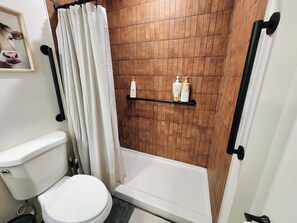 A bathroom with a toilet, a shower with a curtain, and a shelf with toiletry bottles. - Meet Don - A Modern, Zero-step, Pet-friendly home in Rochester (Rochester)