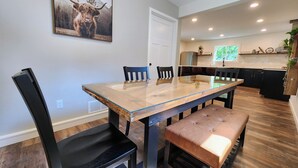 A dining area with a glass-top table, black chairs, and a brown bench. There is a kitchen in the background with a refrigerator and a window. - Meet Don - A Modern, Zero-step, Pet-friendly home in Rochester (Rochester)