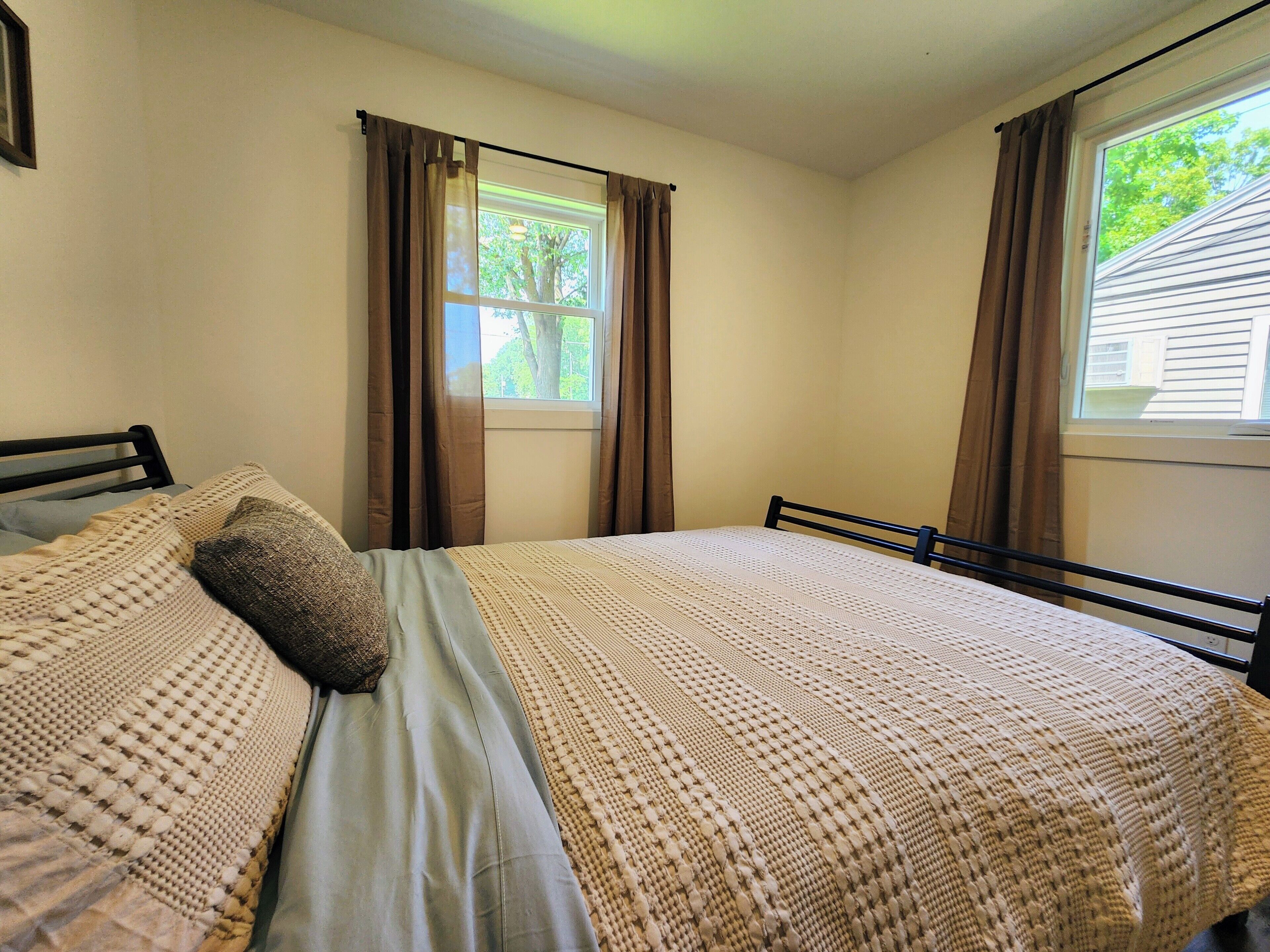 A bedroom with a bed, two windows with curtains, and a view of trees outside.