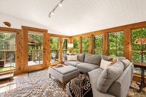 A cozy living room with a sectional sofa, a patterned rug, and large windows offering a view of the outdoors.