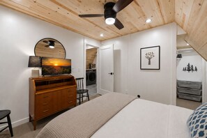 Una camera da letto con un letto, una cassettiera, una sedia, una ventola a soffitto e un quadro.