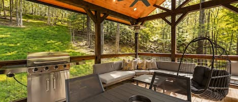 Una terraza al aire libre con una parrilla, zona de estar y sillón colgante.