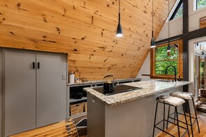 Una cucina con soffitto in legno, piano di lavoro in granito, bollitore e uno sgabello da bar.
