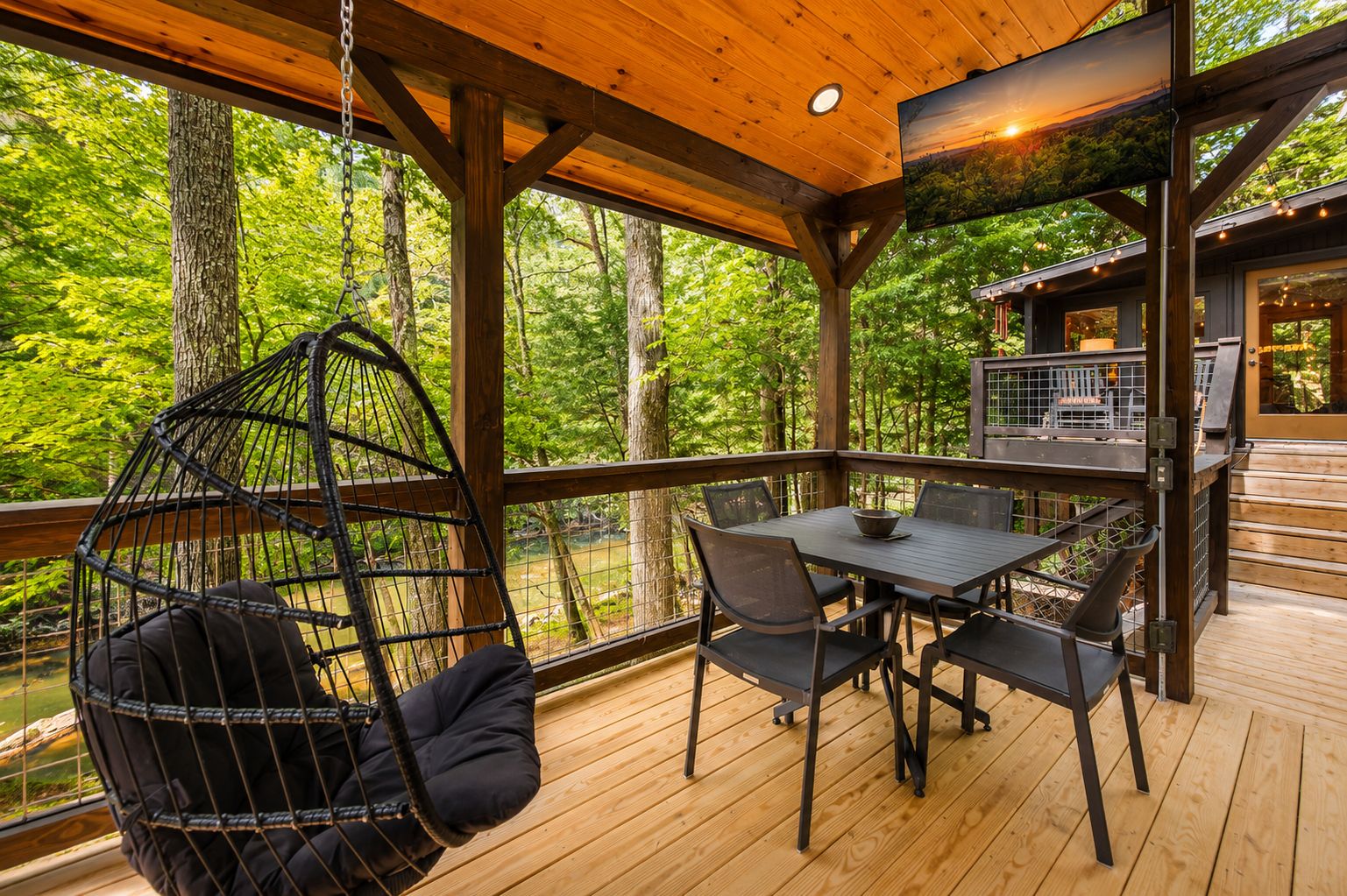 A wooden deck with a hanging chair, a table with chairs, and a view of the forest.