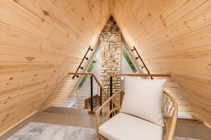 Un interno in legno con una parete in pietra, una sedia di legno con cuscino e una scala con ringhiere nere.