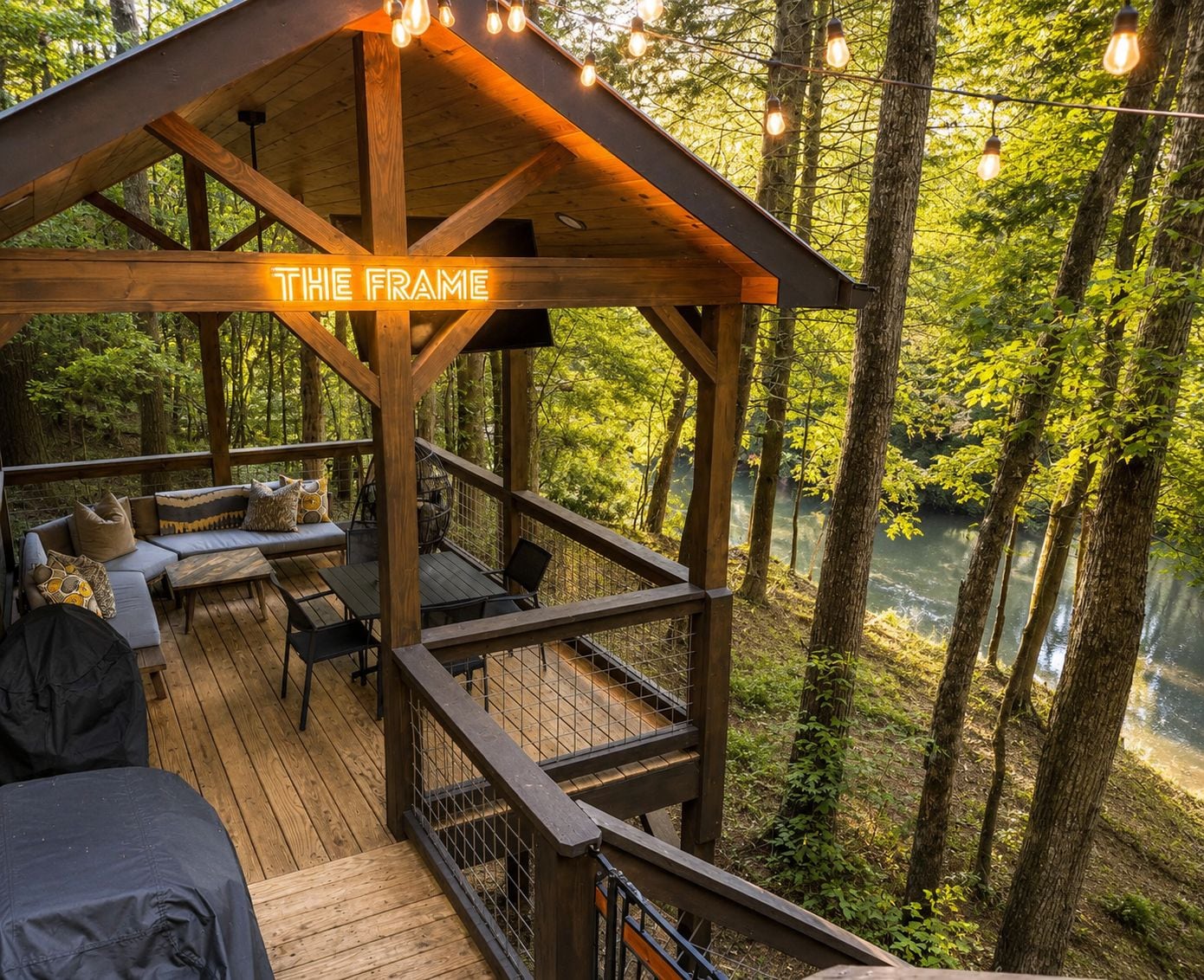 A wooden deck with a covered seating area, surrounded by trees and a body of water.