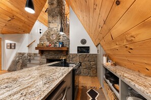 A kitchen with a stone fireplace, wooden ceiling, granite countertops, and a built-in oven.