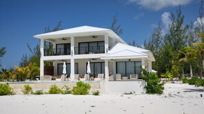 A two-story beachfront property with a covered outdoor seating area and a pool.