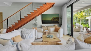 Un salon moderne avec un escalier en bois, un grand tableau et une vue sur l’extérieur.