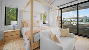Quarto moderno com cama de dossel, área de estar com poltrona e vista para o exterior.