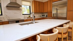 A modern kitchen with a marble countertop, stainless steel appliances, wooden cabinets, and a built-in sink.
