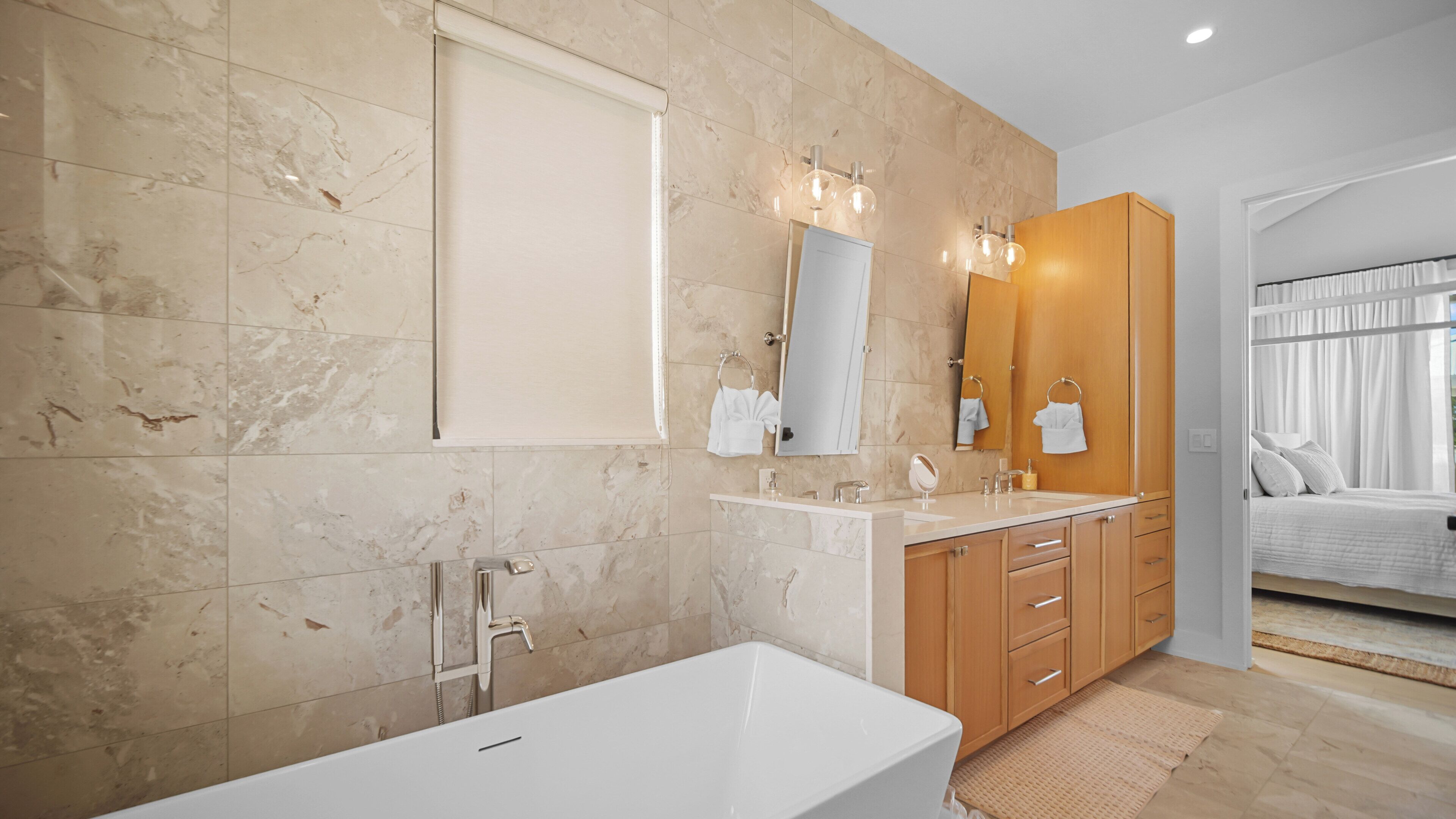 A modern bathroom with a bathtub, double vanity, and a large mirror.