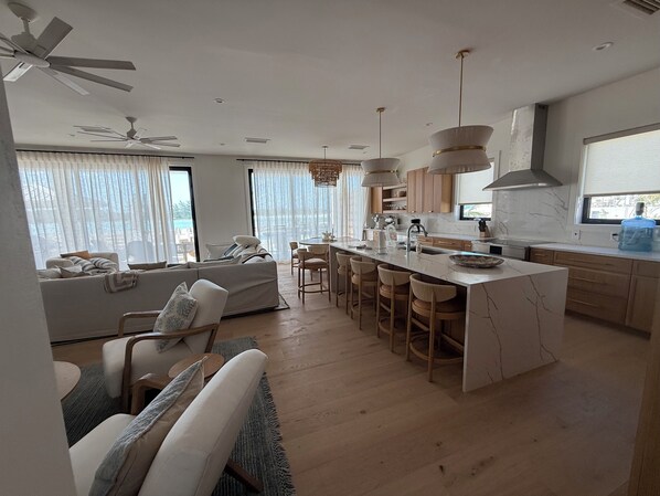 A modern kitchen with a central island, bar stools, and a dining area with a sofa and chairs.