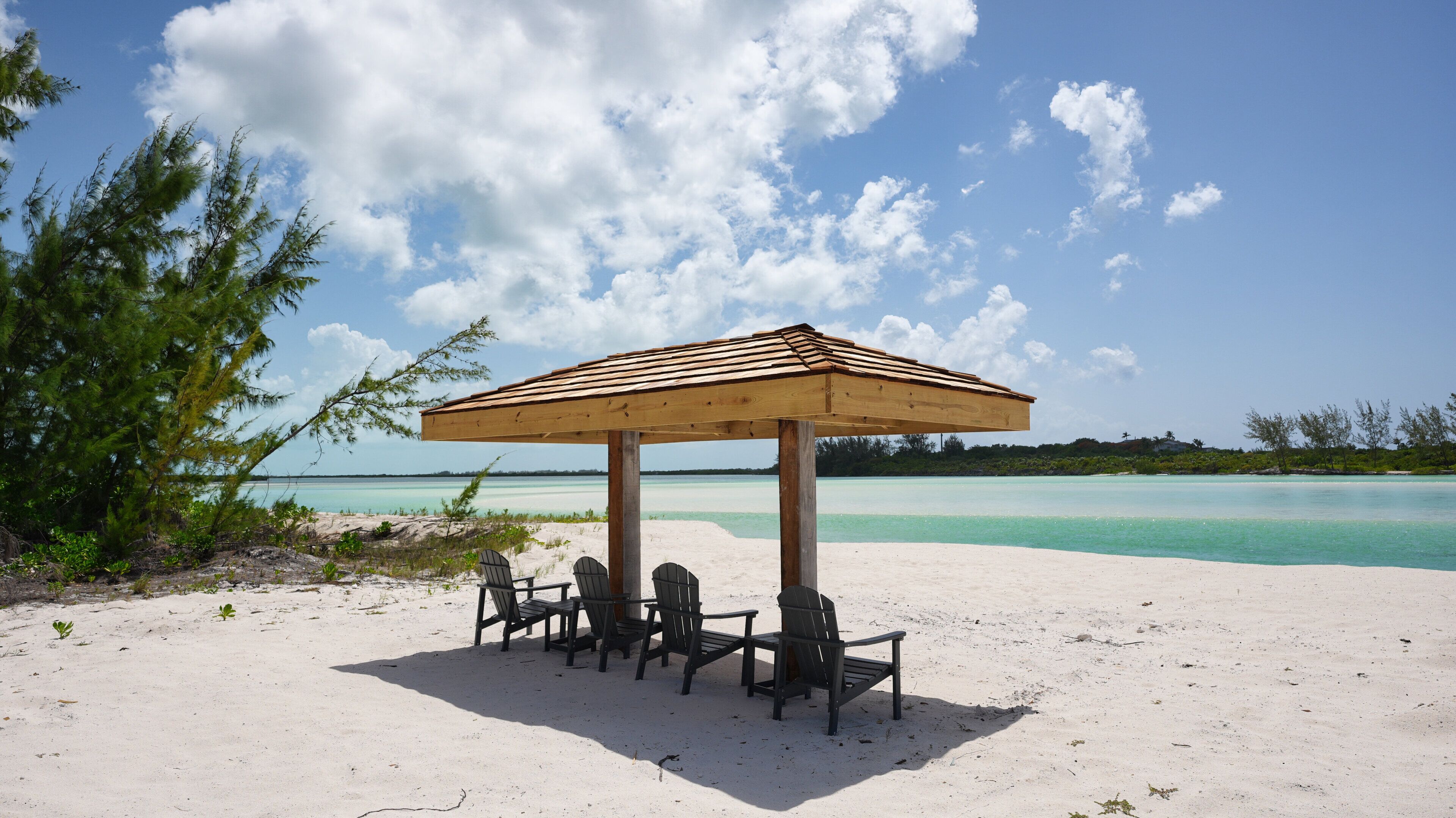 A beach with a wooden gazebo, four chairs, and a view of the sea.